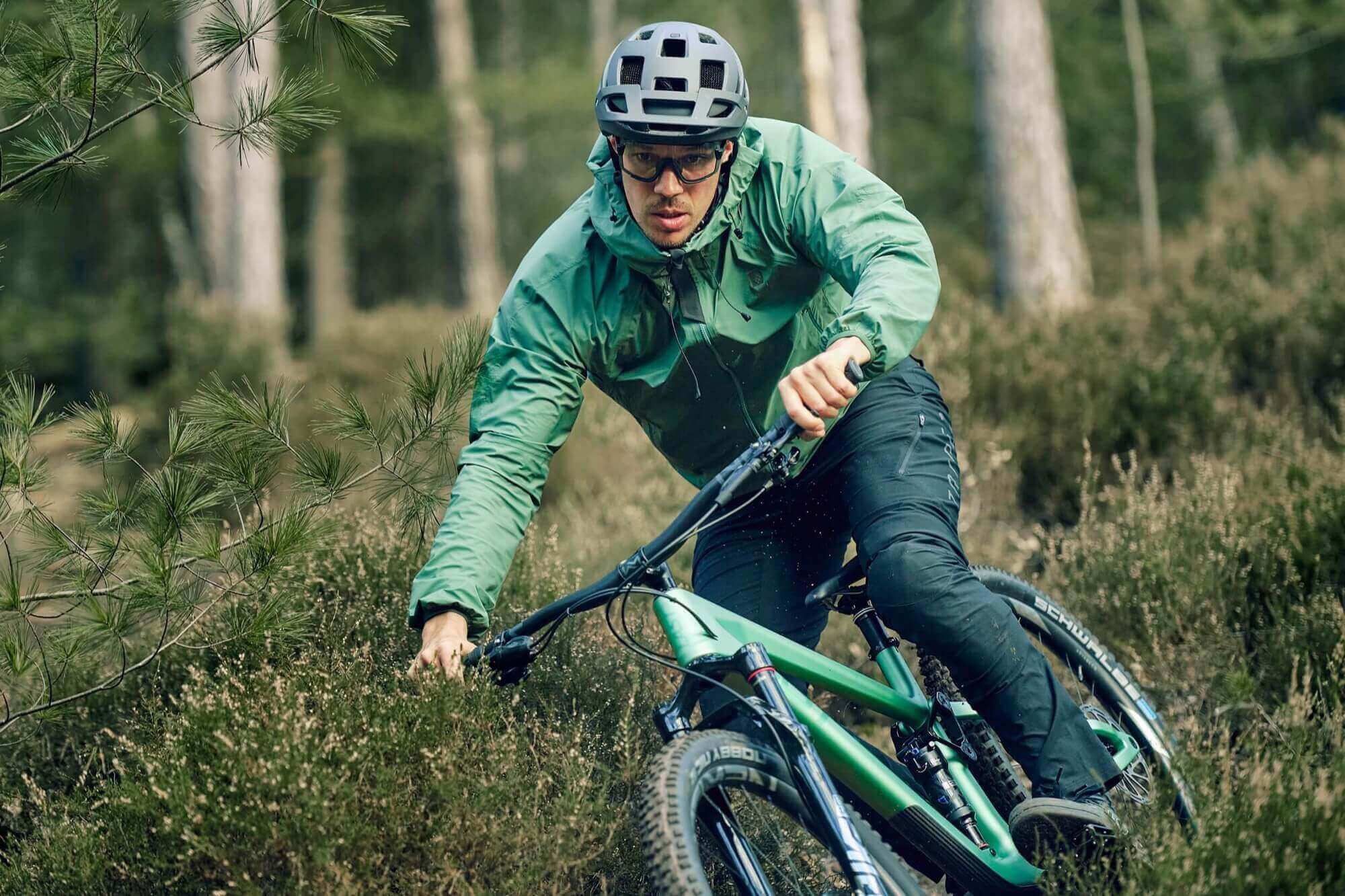 Ein Mann fährt mit dem Fahrrad im Wald - Men&#39;s BUEX Pro 2.0. Robuste MTB Hose aus Bio-Nylon auf Basis von Rizinus Öl. Hochelastisch und extrem abriebfest. Dynamischer, bewegungsoptimierter Schnitt mit breitem Bund für sicheren Halt. Gürtelschlaufen, 2 Taschen vorne und 1 Zip-Tasche am Bein. Vorgeformte Kniepartie für Protektoren und Belüftungsöffnungen hinten. Reflektierende Elemente. TRIPLE2 - Nachhaltige Radbekleidung aus dem Norden.