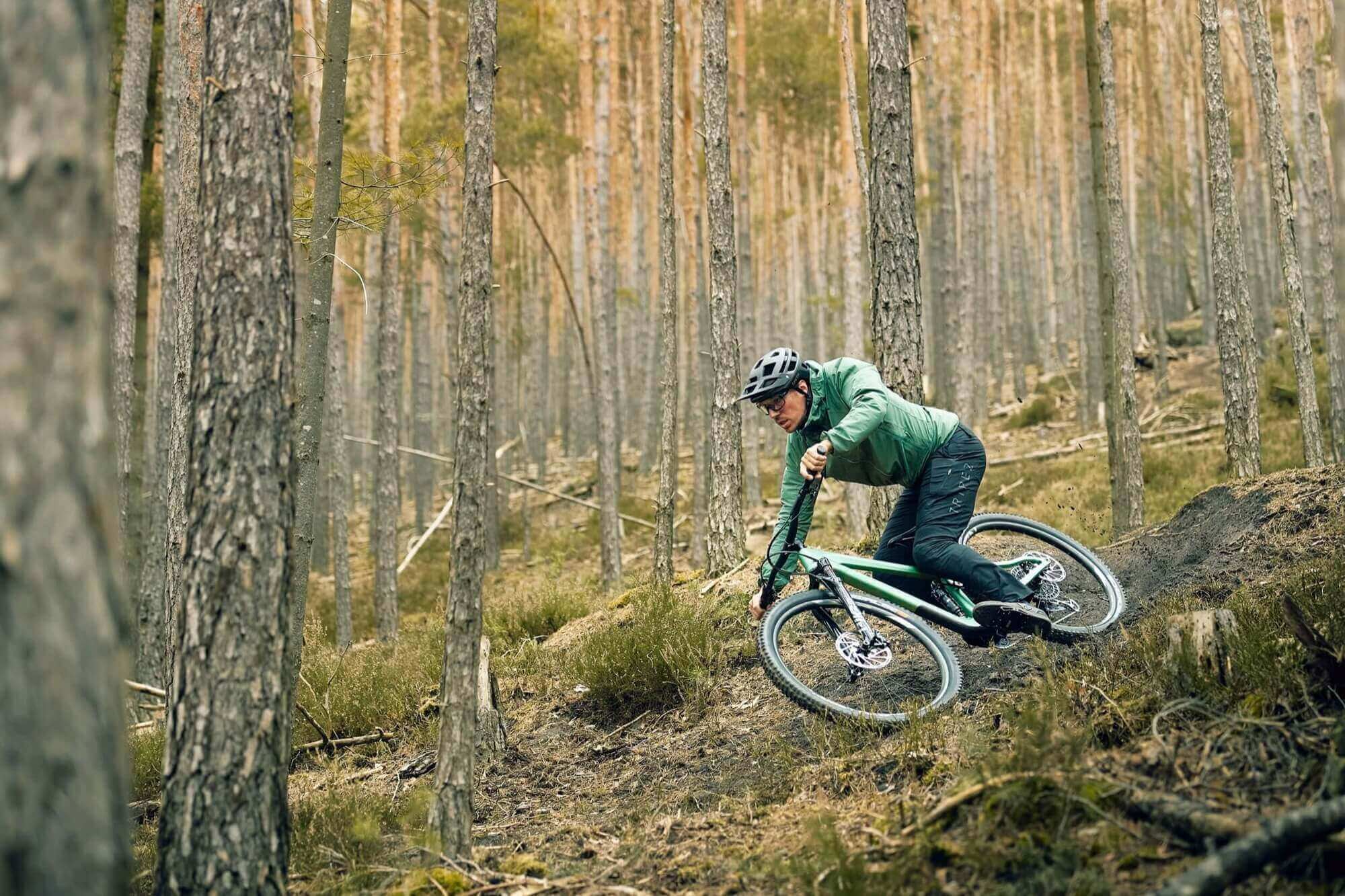 Ein Mann fährt mit dem Fahrrad im Wald - Men&#39;s BUEX Pro 2.0. Robuste MTB Hose aus hochelastischem 4-Wege-Stretch-Material. Hergestellt aus Bio-Nylon auf Basis von Rizinus-Öl. Extrem abriebfest. Dynamischer, bewegungsoptimierter Schnitt. Breiter Bund für sicheren Halt. Gürtelschlaufen. 2 Taschen vorne. 1 Zip-Tasche am Bein. Vorgeformte Kniepartie für Protektoren. Gelaserte Belüftungsöffnungen am Knie hinten. Reflektierende Elemente. TRIPLE2 - Nachhaltige Radbekleidung aus dem Norden.