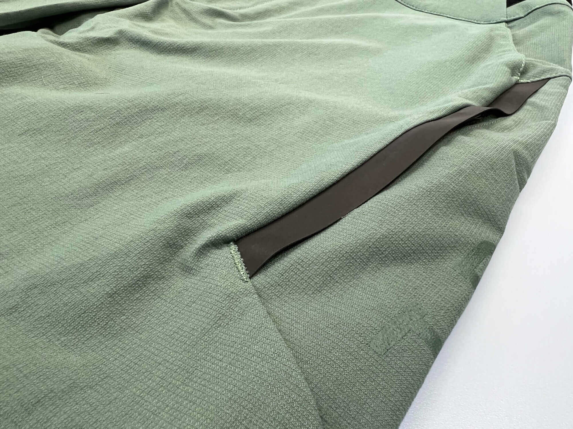 Eine Nahaufnahme einer grünen Jacke aus hochelastischem 4-Wege-Stretch-Material. Hergestellt aus Bio-Nylon auf Basis von Rizinus-Öl. Extrem abriebfest und mit dynamischem, bewegungsoptimiertem Schnitt. Mit breitem Bund für sicheren Halt, Gürtelschlaufen und mehreren Taschen. Reflektierende Elemente sorgen für Sichtbarkeit. Robuste MTB Hose für jeden Einsatzbereich. TRIPLE2 - Nachhaltige Radbekleidung aus dem Norden.